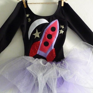 Soft Black 90% cotton, 10% lycra long sleeve black leotard. 
Violet and Red spaceship applique made from recycled felt with red sparkle fabric jet engines. 
 Crescent moon and stars made from white sparkle fabric
Violet and white attached tutu skirt.