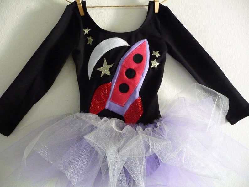 Soft Black 90% cotton, 10% lycra long sleeve black leotard. 
Violet and Red spaceship applique made from recycled felt with red sparkle fabric jet engines. 
 Crescent moon and stars made from white sparkle fabric
Violet and white attached tutu skirt.