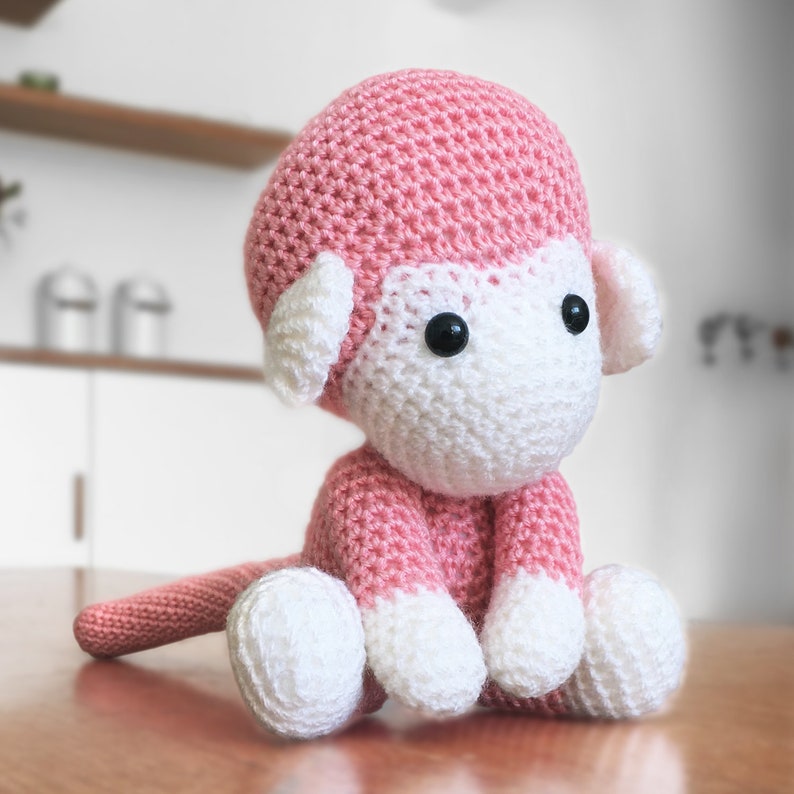 Amigurumi monkey, crocheted in baby pink yarn, sitting on the table.