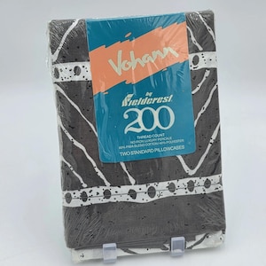 May include: A packaged set of two standard pillowcases. The pillowcases have a dark brown background with a white abstract pattern. The packaging includes a blue and orange label with the brand name "Vohann by Fieldcrest 200".