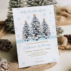 May include: A baby shower invitation with a winter theme. The invitation features three snow-covered pine trees with gold ornaments and the text "baby it's cold outside". The invitation also includes the text "Join us for a baby shower honoring Catherine Williams, Saturday November 17th | 10:00 pm, The William's Residence, Palmetto Springville 6216 Georgia, RSVP to Sandra 000-000-000, Registered at Target & Amazon".