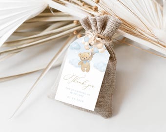 May include: A small burlap bag with a thank you tag attached. The tag features a watercolor illustration of a teddy bear holding balloons with clouds in the background. The text on the tag reads "Thank you. For showering us with love. 03.12.2023."