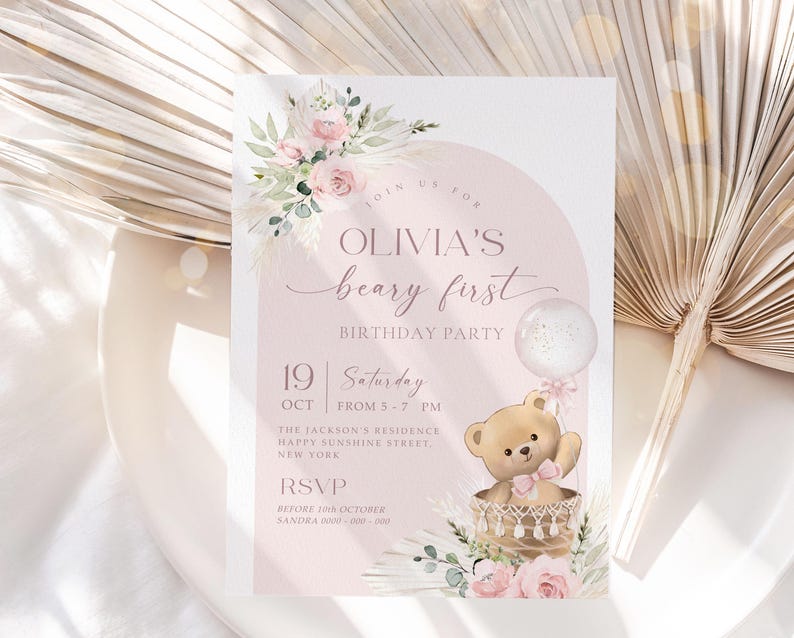 Pink floral first birthday invitation featuring a teddy bear in a basket, pastel flowers, and a balloon for a baby girl's Beary First birthday party
