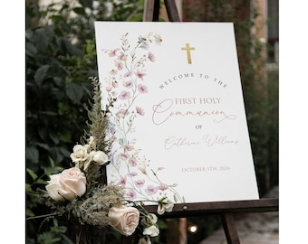 May include: A white sign with a floral design and gold cross. The sign reads "Welcome to the First Holy Communion of Catherine Williams October 31st, 2024".