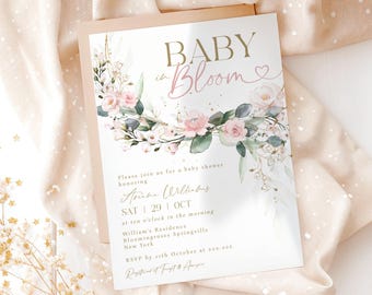 May include: Baby shower invitation with the words "BABY in Bloom" in gold and pink script. The invitation features a floral wreath with pink roses and green leaves. The text includes the honoree's name, date, time, and location.