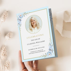 May include: A light blue memorial card with a gold border and a watercolour floral design. The card features a photo of a woman and the text "Celebrating the life of Clarissa Williams, October 20, 1985 - July 13, 2018, Sunday, July 14, 2018 at 6 PM, Saint Maria Church New York, NY."