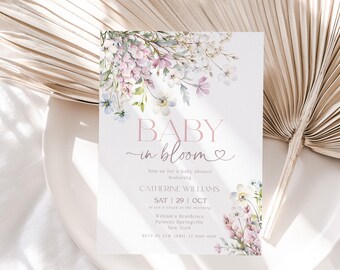 May include: A baby shower invitation featuring the words "BABY in bloom" in pink. The design includes watercolour floral arrangements in pink, purple, and white. The invitation provides details such as the honoree's name, date, time, and location.