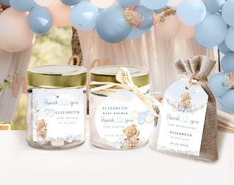 May include: Baby shower favors featuring a teddy bear design. The favors include glass jars with gold lids, a round label, and a burlap bag with a tag. Each item has a "Thank You" message, the name "Elizabeth", and the date.