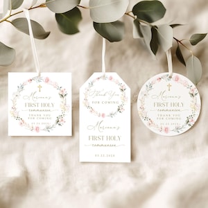 May include: Three white First Holy Communion gift tags with floral wreath designs and the text "Mariana's First Holy Communion". The tags are square, tag-shaped, and circular, each with a white ribbon.