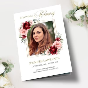 May include: A white memorial card with a gold frame surrounding a photo of a woman. The photo is surrounded by a floral arrangement of burgundy and pink roses, greenery, and eucalyptus. The text "IN LOVING Memory" is at the top of the card. The text "JENNIFER LAWRENCE" is below the photo. The dates "OCTOBER 20, 1985 - JULY 13, 2018" are below the name. The text "SUNDAY, JULY 14, 2018 AT 6 PM" and "SAINT MARIA CHURCH NEWYORK, NY" are at the bottom of the card.