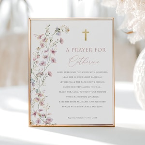 Puede incluir: Una impresión rectangular en un marco dorado fino con una cruz dorada, ilustraciones de flores silvestres rosas y moradas, y el texto A PRAYER FOR Catherine, seguido de una oración y la fecha Baptised October 19th, 2025, sobre un fondo blanco.