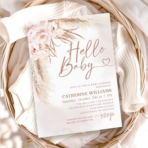 May include: A baby shower invitation with the words "Hello Baby" in a delicate script, adorned with floral and pampas grass accents. The invitation includes details for Catherine Williams' baby shower, set against a soft, neutral background.