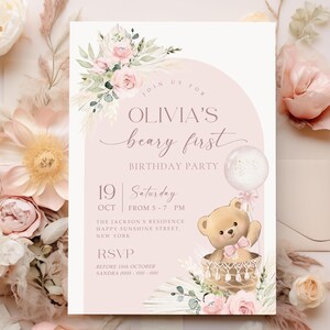 Pink floral first birthday invitation featuring a teddy bear in a basket, pastel flowers, and a balloon for a baby girl's Beary First birthday party