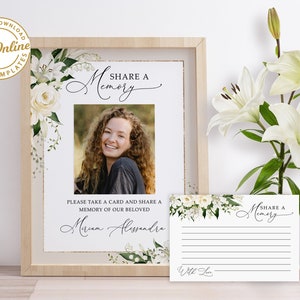 Puede incluir: Un letrero conmemorativo enmarcado con una foto, detalles florales y el texto "Share a Memory". Se incluye una tarjeta a juego. El letrero dice "Please take a card and share a memory of our beloved". El diseño presenta flores blancas.