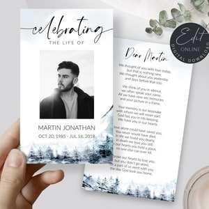May include: A memorial card featuring a black and white photograph of a man. The card has a blue watercolour background with a mountain scene. The text on the card reads "Celebrating the Life of Martin Jonathan Oct 20, 1985 - Jul 16, 2018".