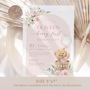 Pink floral first birthday invitation featuring a teddy bear in a basket, pastel flowers, and a balloon for a baby girl's Beary First birthday party