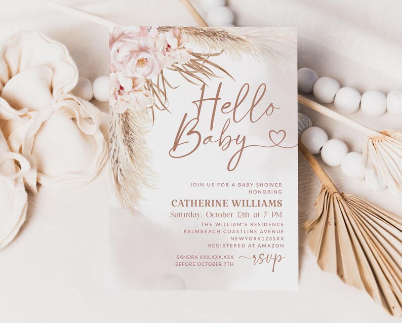 May include: A baby shower invitation with the words "Hello Baby" in a stylish script font. The invitation features floral and pampas grass accents in soft pink and beige tones. Details include the honoree's name, date, time, and location.