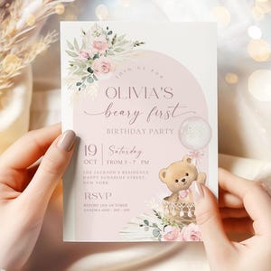 Pink floral first birthday invitation featuring a teddy bear in a basket, pastel flowers, and a balloon for a baby girl's Beary First birthday party