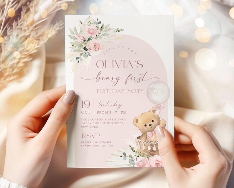 Pink floral first birthday invitation featuring a teddy bear in a basket, pastel flowers, and a balloon for a baby girl's Beary First birthday party