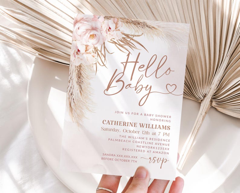 May include: A baby shower invitation with the words "Hello Baby" in elegant script. The invitation features floral and pampas grass accents in soft pink and beige tones. Details include the honoree's name, date, time, and location.