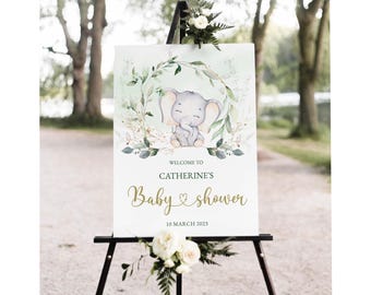 May include: Welcome to Catherine's Baby Shower sign with a green leafy wreath and a cute gray elephant illustration. The sign is on a wooden easel and has a gold heart and the date 10 March 2023.