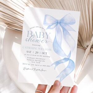 May include: A baby shower invitation with a watercolor-style light blue bow and ribbons. The invitation includes the text "BABY shower" and details for Catherine Williams' baby shower, including the date, time, and location.