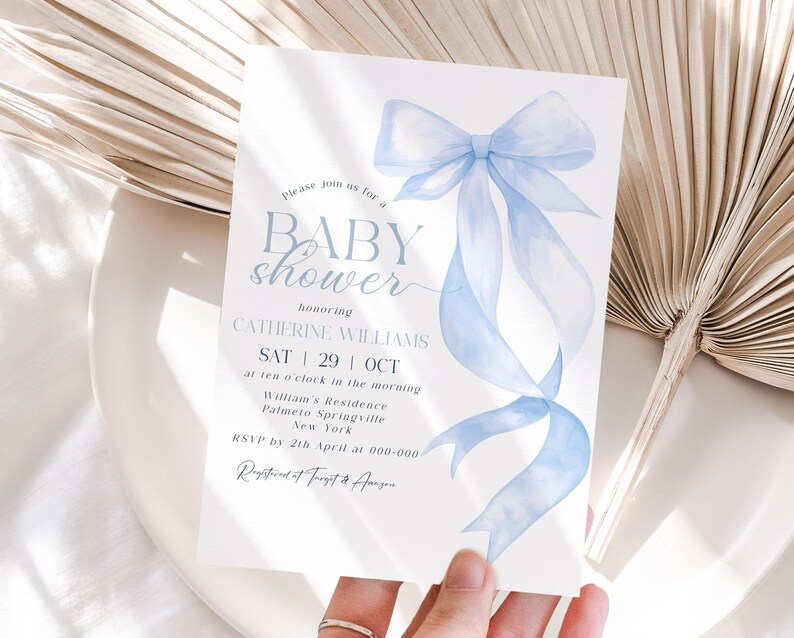 May include: A baby shower invitation with a watercolor-style light blue bow and ribbons. The invitation includes the text "BABY shower" and details for Catherine Williams' baby shower, including the date, time, and location.