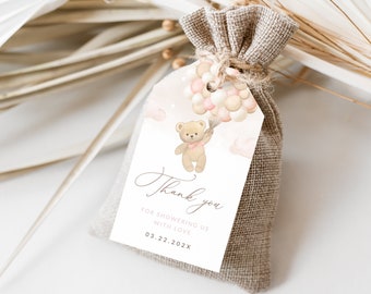 May include: A small burlap gift bag with a tag featuring a teddy bear holding balloons. The tag reads "Thank you" and "For showering us with love". The teddy bear is light brown with a pink bow.