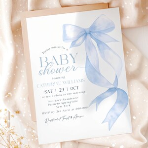 May include: A baby shower invitation featuring a light blue watercolor bow and ribbon design. The invitation includes the text "BABY shower" and details for Catherine Williams' baby shower, including the date, time, and location.