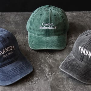 Könnte beinhalten: Drei Baseballkappen in verschiedenen Farben mit besticktem Text. Die erste Kappe ist grün mit "Custom Embroidery" in weißer Schrift. Die zweite Kappe ist blau mit "Grandpa Est. 2024" in weißer Schrift. Die dritte Kappe ist grau mit "Forum" in weißer Schrift.