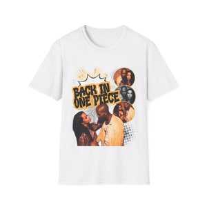 May include: White t-shirt with a graphic design. The design features the text "BACK IN ONE PIECE" in a comic book style, alongside sepia-toned images of people, giving a vintage feel.