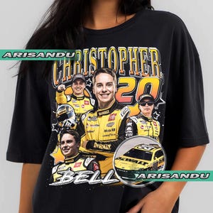 May include: Black t-shirt featuring a graphic of Christopher Bell, a NASCAR driver, with the number 20. The design includes multiple images of Bell in his racing uniform, along with the DeWalt logo and car. The text "CHRISTOPHER BELL" is prominently displayed.