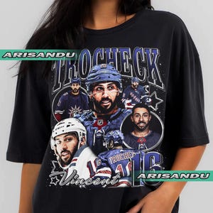 May include: Black t-shirt featuring a collage of images of a hockey player in a blue and white uniform. The shirt includes the name "TROCHECK" in large letters and the name "Vincent" with the number "16".