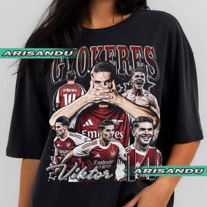 May include: Black t-shirt featuring a collage of images of a soccer player in a red and white uniform. The shirt has the name "GYOKERES" and "Viktor" printed on it, along with the number 10 and 14. The brand name "ARISANDU" is also printed on the shirt.