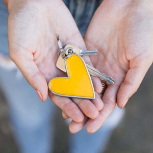 Könnte beinhalten: Ein gelber herzförmiger Schlüsselanhänger mit einem silbernen Ring und zwei daran befestigten Schlüsseln.