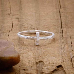 Puede incluir: Un anillo de plata con textura martillada y un diseño de cruz simple.