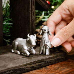 May include: A nativity scene set with a silver ox, a silver shepherd figure holding a drum, and a wooden stable.