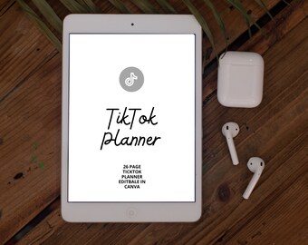 May include: A white tablet computer with a blank screen displaying the text "TikTok Planner" and the TikTok logo. The text below the title reads "26 Page TikTok Planner Editable in Canva". The tablet is on a wooden surface with a pair of white wireless earbuds and a white charging case.