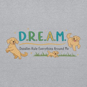 Può includere: Una maglietta grigia con un design grafico che presenta la parola "D.R.E.A.M." con tre cani barboncini. Il testo sotto la parola "DREAM" dice "Doodles Rule Everything Around Me".