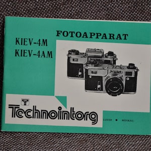 Op de afbeelding: Een groene handleiding voor een Kiev-4M en Kiev-4AM camera. De handleiding bevat een zwart-wit afbeelding van de camera en de tekst "FOTOAPPARAT" en "Technointorg USSR MOSKAU".