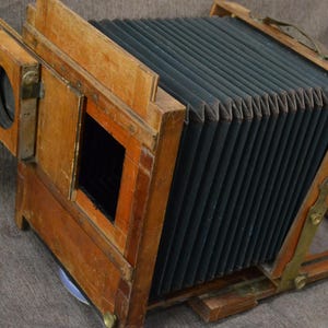 May include: A vintage wooden camera with a bellows system and a brass lens. The camera has a wooden frame and a black bellows. The camera is in good condition and has a classic look.