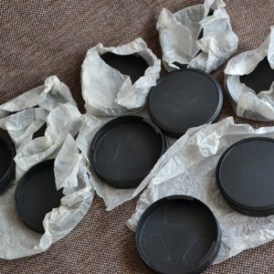 May include: A set of eight black lens caps for cameras, wrapped in white tissue paper.