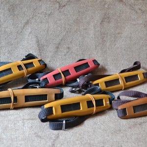 Puede incluir: Seis llaveros rectangulares de madera de colores con correas negras. Cada llavero tiene un color y un diseño diferente.