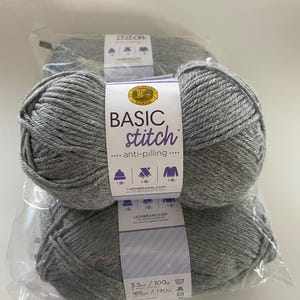 May include: Three skeins of grey Basic Stitch anti-pilling yarn. Each skein is wrapped in clear plastic and has a label with the Lion Brand logo, the yarn weight of 100g, and the length of 170m.