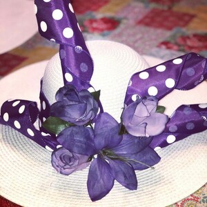 以下が含まれることがあります： 白い麦わら帽子に、白のドット模様の紫のリボンと紫の花が飾られています