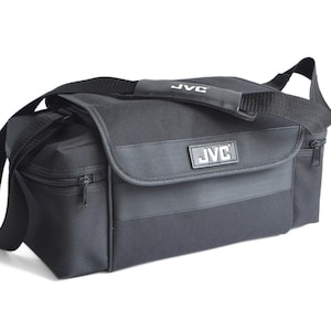 May include: Black rectangular shoulder bag with a flap and a shoulder strap. The bag has a zip closure and a handle on top. The brand name "JVC" is displayed on the front of the bag in a silver rectangle.
