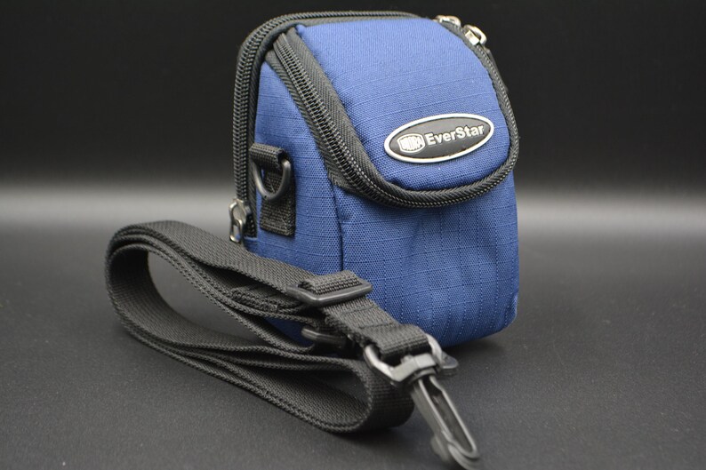 May include: A blue camera bag with a black strap. The bag has a zippered closure and a small metal emblem that reads "EverStar". The strap is adjustable and has a metal clasp.
