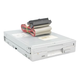 Puede incluir: Una disquetera interna de color gris claro con una placa frontal rectangular, un pequeño botón de expulsión y una luz indicadora de estado. Un cable plano gris plegado con conectores de plástico negro descansa sobre la carcasa.
