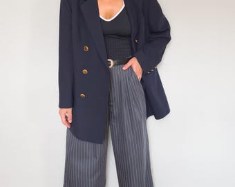 May include: A navy blue double-breasted blazer with gold-toned buttons, paired with a black tank top featuring a white trim and charcoal gray wide-leg trousers with vertical white pinstripes, held together by a black belt with a gold buckle.
