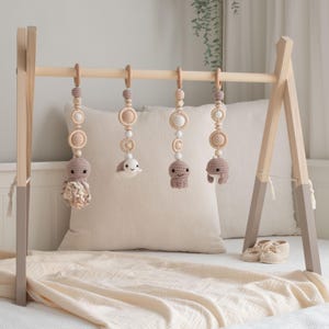May include: A wooden baby play gym with four hanging toys. The toys are crocheted and feature a variety of sea creatures, including an octopus, a turtle, and a whale. The play gym is a light wood color and has a white and beige blanket underneath.